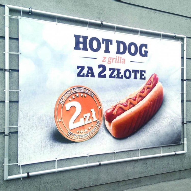 baner reklamowy z hot dogiem i napisem „Hot dog z grilla za 2 złote” zamocowany na ścianie