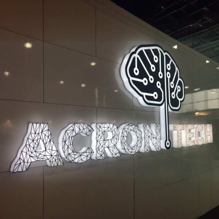 Białe litery 3D z podświetleniem LED i geometrycznym wzorem, zamontowane na gładkiej ścianie w nowoczesnym wnętrzu firmowym.