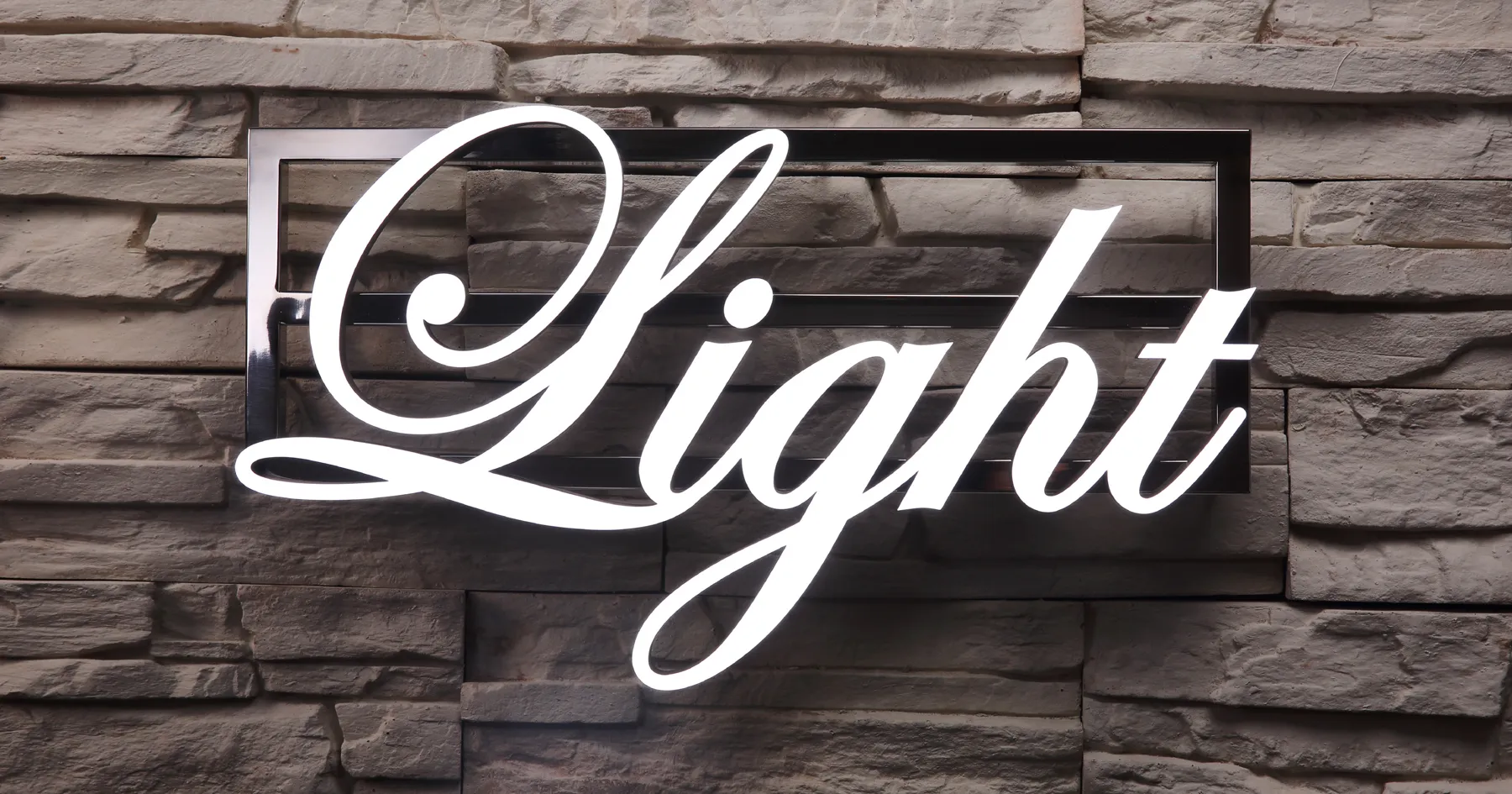 Podświetlany napis LEDON „Light” zamontowany na tle kamiennej ściany, wykonany z połyskującego metalu i mlecznej plexi z efektem LED
