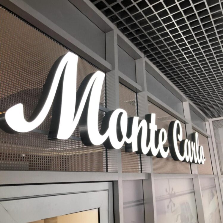 Podświetlany napis LEDON „Monte Carlo” zamontowany na elewacji wewnętrznej, wykonany z aluminium i mlecznej plexi z równym, jasnym światłem LED.