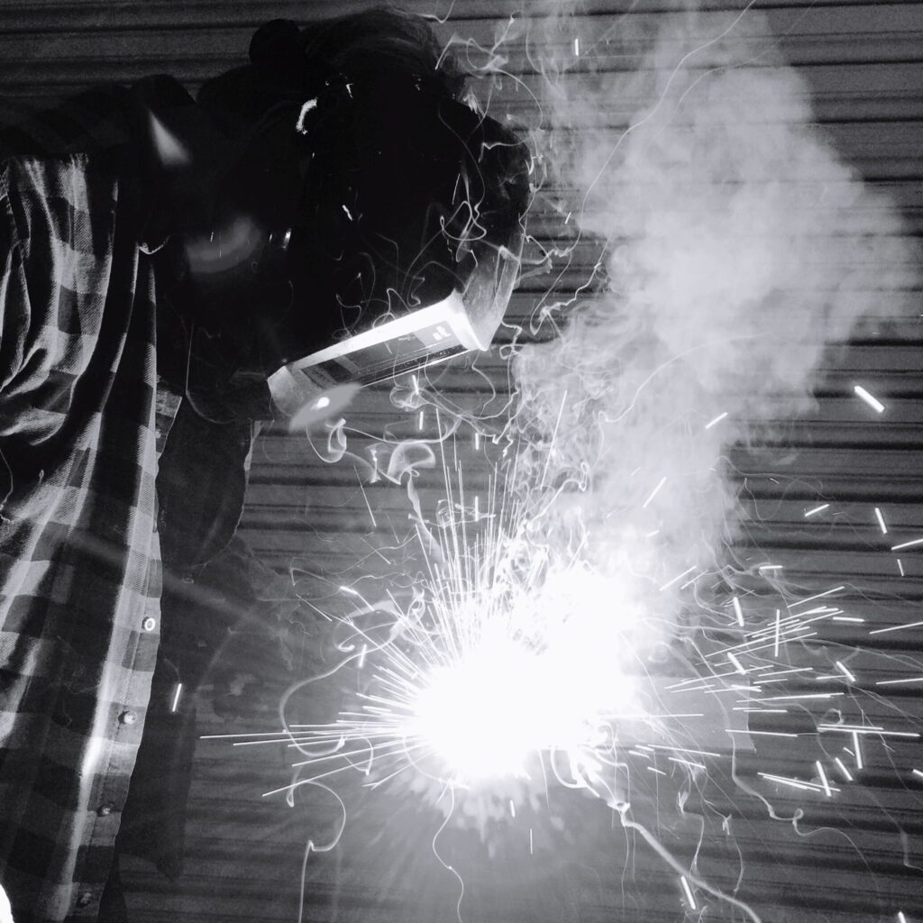 Spawacz w przyłbicy ochronnej pracujący nad elementem stalowym.