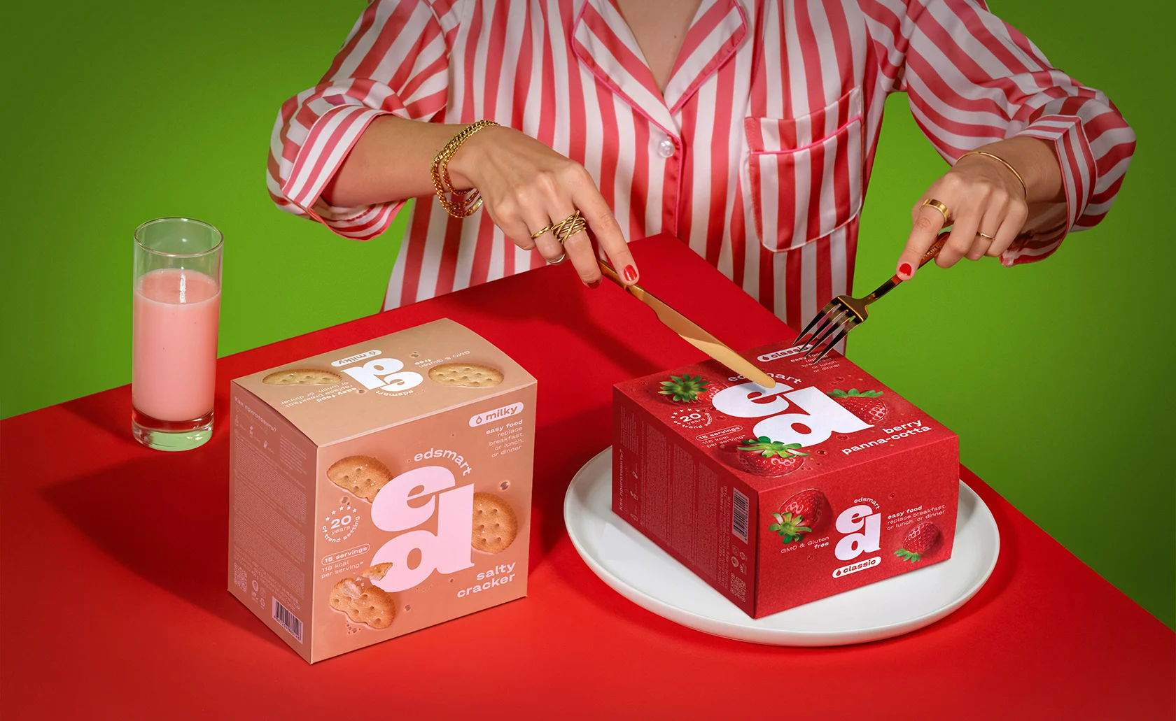 Dwa opakowania koktajli Edsmart w aranżacji stołowej z naczyniami i napojem.