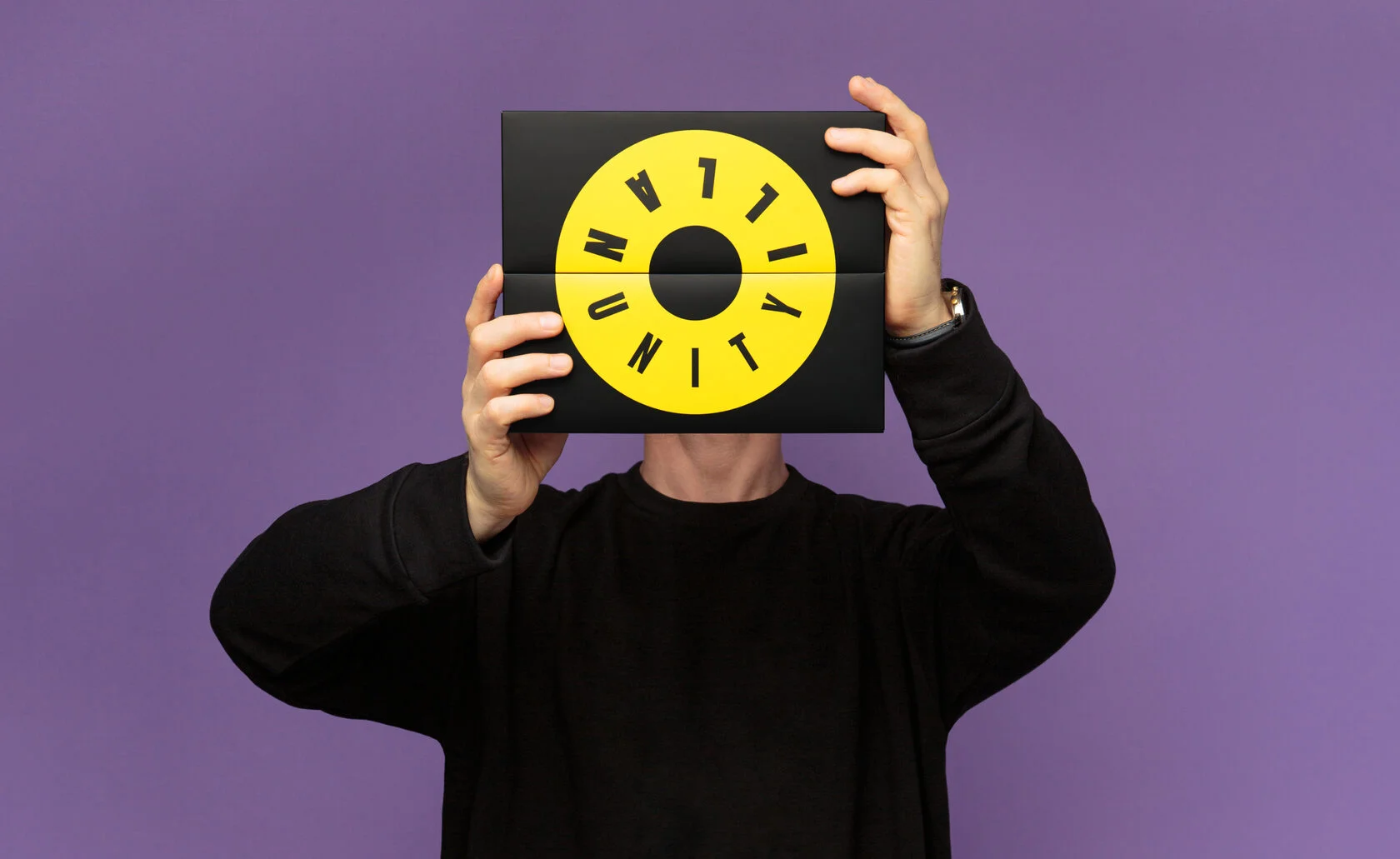 Osoba trzyma czarną planszę z żółtym okrągłym logotypem Illan Unity na tle fioletu.